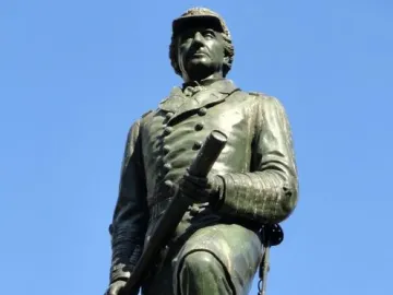 Admiral David G. Farragut statue in bronze with a green patina, holding a telescope against a blue sky.