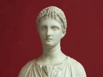 Artemis Diadoumena marble torso with draped folds and braided hair against a red background.