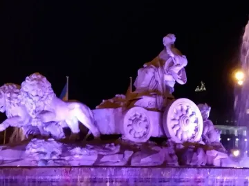The Cibeles Fountain at night, lit in purple with water spraying from the fountain.