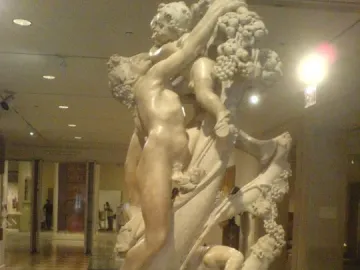 Marble sculpture of A Faun Teased by Children showing a muscular nude figure reaching up toward grapes and a child, with another child near the base.