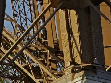 Gilded bust of Gustave Eiffel on a stone pedestal beneath the Eiffel Tower\'s metal framework.