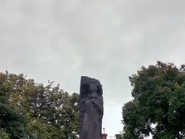 Karl Marx Monument on a tiered stone base in a paved plaza with trees behind it.