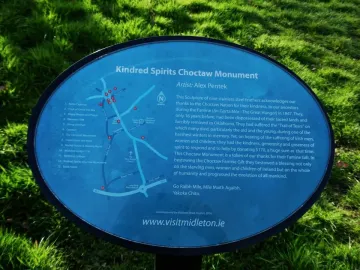 Blue informational plaque for the Kindred Spirits Choctaw Monument with white text and a small map beside grass.