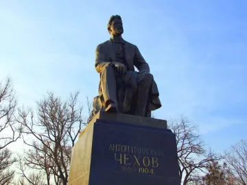 Chekhov Monument, a bronze seated statue of a bearded man on a pedestal against a blue sky