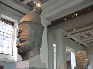 Colossal Head of Amenhotep III with a speckled stone arm displayed on supports in the foreground.