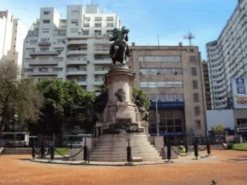 Bronze equestrian monument to Giuseppe Garibaldi on a tall stone pedestal in a city plaza, with trees and surrounding buildings.