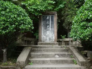 Weathered stone stele with Chinese inscriptions at the top of stone steps, surrounded by green foliage at Huangze Monastery.