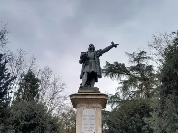 Monument to Columbus showing a bronze figure in period attire pointing outward on a tall stone pedestal.