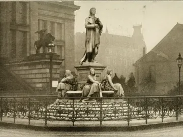 Schiller Monument with a standing man at the center, surrounded by three allegorical female figures and an ornate fence.