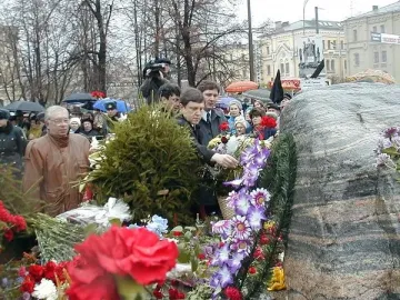 Solovetsky Stone covered with floral wreaths and bouquets as people gather around the memorial.