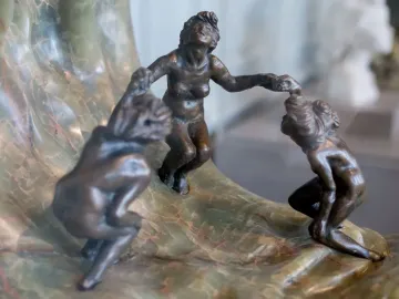 Three dark bronze nude figures holding hands on The Wave sculpture with a curling marbled stone base.