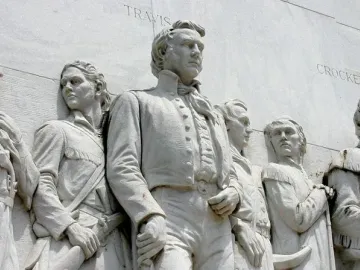 Relief figures on the Alamo Cenotaph with the names Travis and Crockett etched in the stone.