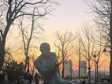 Fisherman Fountain statue wrestling with a large snake in a park at sunset.