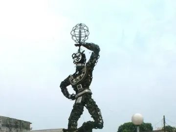 La Nouvelle Liberté sculpture rising on a stone base in an urban square, with one arm raised holding a spherical metal form.