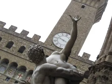 Rape of the Sabine Women sculpture seen from below, with a muscular male figure lifting a nude woman in front of a clock tower.