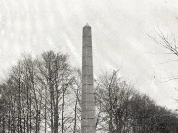 The Needle, a tall stone monument on a tiered base in a grassy clearing with bare trees behind it.