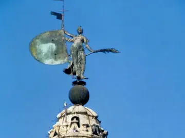 The Giraldillo statue holding a shield and palm branch atop the Giralda tower against a blue sky.