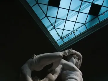 Hercules and Lychas marble sculpture lit against a dark background with a blue skylight above.