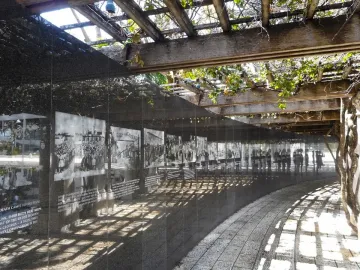 Curved dark wall at the Holocaust Memorial displaying historical photographs and text beneath a wooden pergola.