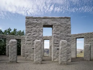 Maryhill Stonehenge with rough gray stone pillars and lintels framing a view of dry rolling hills under a blue sky.