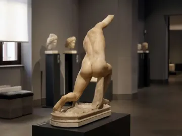 Back view of the Subiaco Ephebe sculpture on a pedestal in a museum gallery, missing its head and arms.