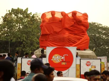 Anti Terrorism Raju Memorial Sculpture covered in bright orange fabric, with human-like figures visible at the top and a crowd in front.