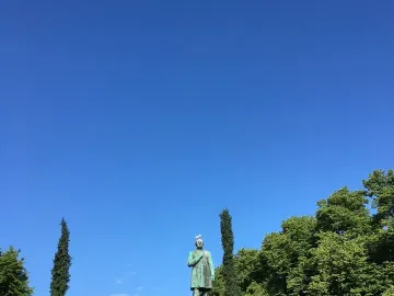 Johan Ludvig Runeberg statue on a stone pedestal with trees and a bright blue sky behind it, topped by a white bird.