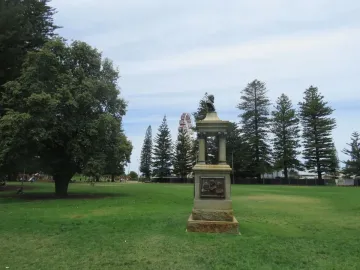 Maitland Brown Memorial stone monument with a bust and relief figures, with a Ferris wheel in the background.