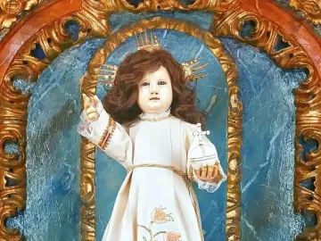Santo Niño de Cebú statue in an ornate blue and gold shrine, dressed in a cream gown and holding a cross-topped orb.