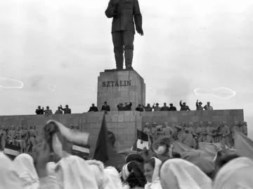 Stalin Monument with a towering statue on a stepped stone pedestal, with crowds gathered below and around the base.