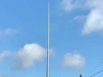 The Spire towers over a busy Dublin street with buses, cars, pedestrians, and surrounding buildings under a blue sky.
