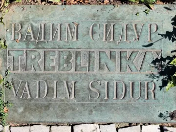 Weathered bronze Treblinka memorial plaque with carved Cyrillic and Latin text set into the ground.