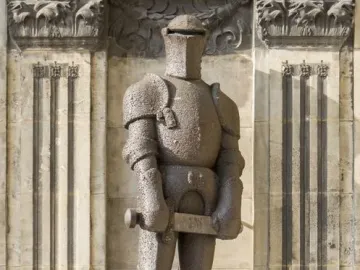 Wehrmann in Eisen, a dark armored knight statue with a hammer, standing on a carved pedestal against a stone facade.