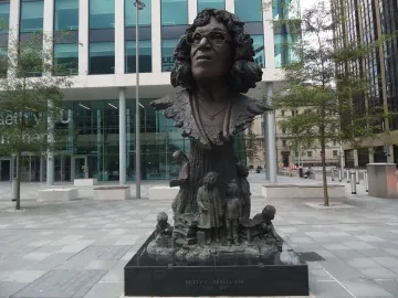 Betty Campbell statue with a smiling bronze bust above figures of children on a tree trunk base.