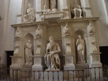 Marble statue of Moses seated with tablets under one arm, his other hand near his chin, with a long beard and horn-like protrusions on his head.