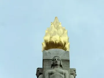 Upper section of the Titanic Engine Room Heroes Memorial with a gilded flame finial above carved female figures.