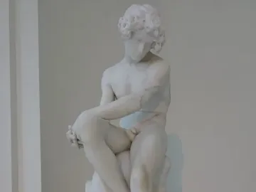 The Exiled, a white marble sculpture of a seated nude male figure with curly hair and a downcast expression.