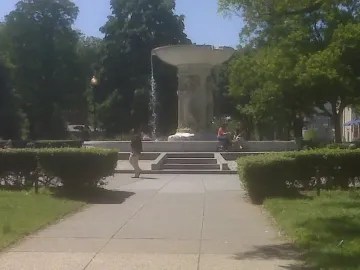 Dupont Circle Fountain in a green park with water flowing from the upper basin and people nearby.