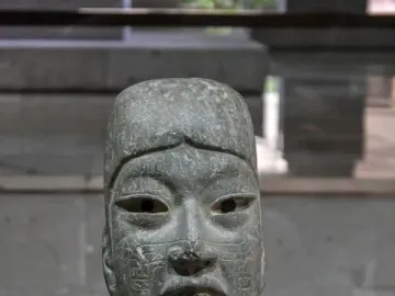 Las Limas Figurine showing a carved stone human figure with glyphs across the face, chest, and arm, holding a smaller figure.