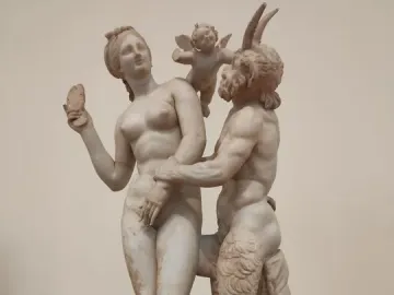 Marble sculpture group of Aphrodite with Pan and Eros, showing a nude female figure resisting a horned, goat-legged Pan while a small winged Eros pushes him away.