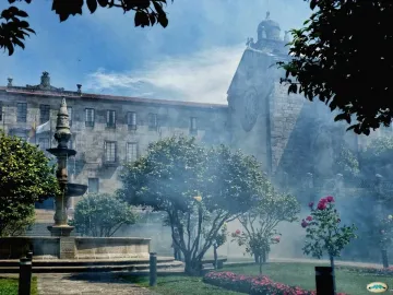 Herrería Fountain with water cascading into a circular stone basin, with trees and mist in the background.