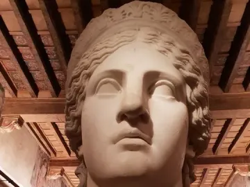 Juno Ludovisi marble head displayed in a room with ornate wooden ceiling and frescoed walls.
