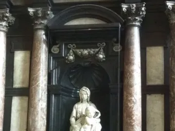 Madonna of Bruges marble sculpture seated with the Christ Child in a dark carved niche behind glass.