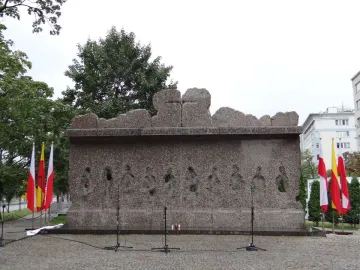 The Monument to Victims of the Wola Massacre, a rugged granite memorial with abstract human figures and circular recesses on its facade.