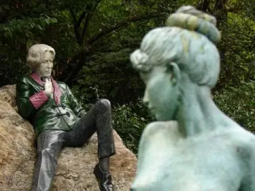 Oscar Wilde Memorial Sculpture showing a reclining male figure in a green jacket beside a pale green nude female figure in the foreground.