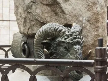 Bronze ram head at the Monument to Viriato, with blue and white ceramic vessels in front of a stone pillar.