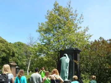 The Eternal Silence sculpture, a tall patinated bronze robed figure on a dark monument in a grassy setting with visitors nearby.