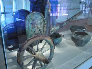 Monteleone Chariot displayed behind glass with a spoked wheel, decorated relief panel, and long shaft visible.