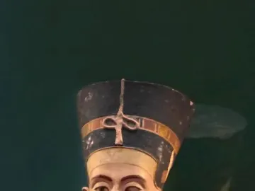 Bust of Nefertiti with a tall blue and gold crown, painted face, and patterned collar against a dark green background.