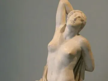 Niobid sculpture in marble, shown kneeling with one arm raised and her head tilted back.